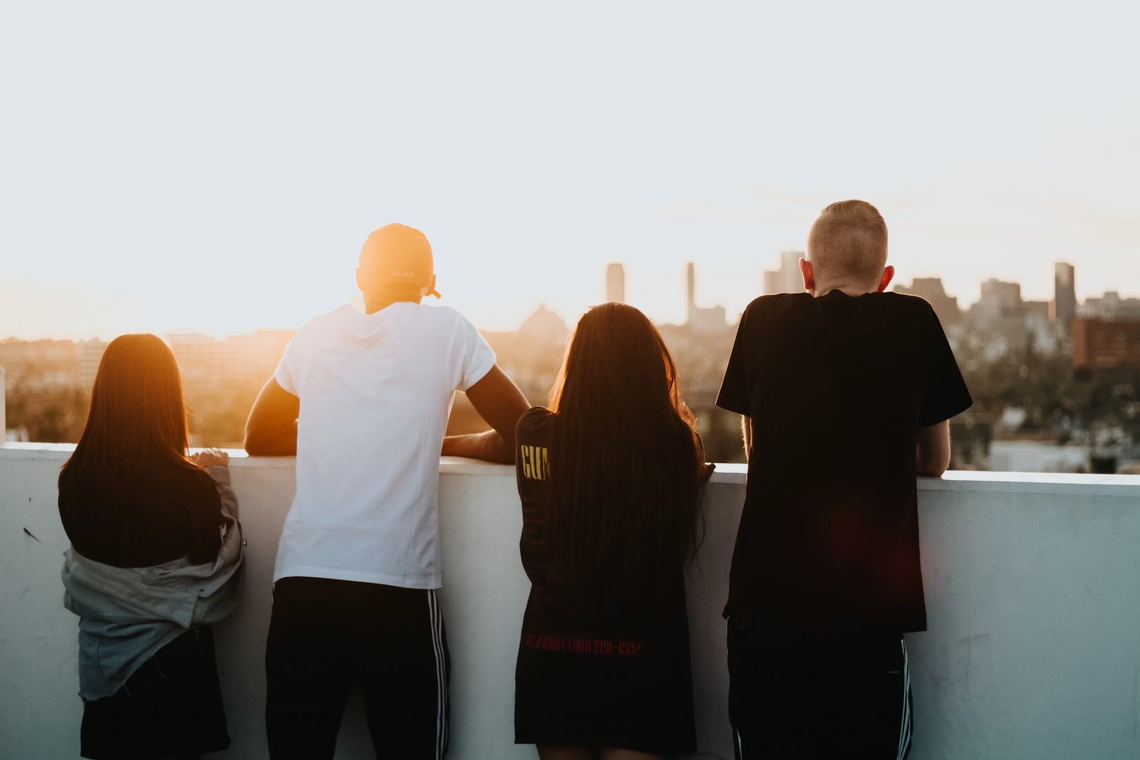 Four young people standing together on a rooftop at sunset, looking out over the city skyline